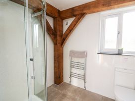 A bathroom with a glass shower enclosure wooden beams a towel rack with a towel a window with a small plant and a toilet at Yr Adfa in Llangeitho near Tregaron
