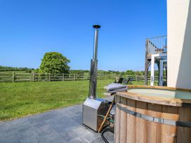 An outdoor hot tub on a patio overlooking a fenced grassy field with chairs and a clear blue sky at Yr Adfa in Llangeitho near Tregaron