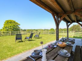 A covered outdoor dining area with a wooden table set with plates and bowls next to a grassy area with lawn chairs and a wooden fence at Yr Adfa in Llangeitho near Tregaron