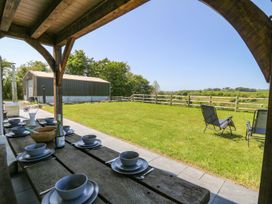 An outdoor covered dining area with a wooden table set for six and lawn chairs on grass at Yr Adfa in Llangeitho near Tregaron