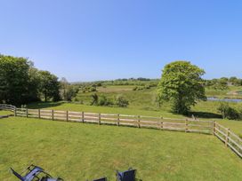 A fenced grassy garden with outdoor chairs and trees overlooking fields and a pond at Yr Adfa in Llangeitho near Tregaron