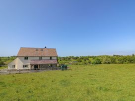 A house with a fenced yard in a green field with trees and hills in the background at Yr Adfa in Llangeitho near Tregaron