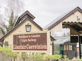 A railway station sign for Welshpool and Llanfair Light Railway at Llanfair Caereinion with station buildings and a green train carriage