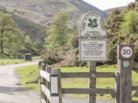 A rural road with wooden fences and National Trust signs in a valley with grassy hills and trees at Carding Mill Valley