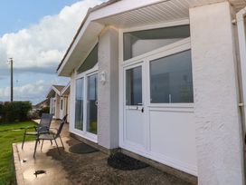 A white house exterior with large windows a door and two chairs on a concrete patio at Chalet 22 in Port Eynon