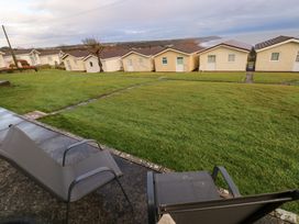 Two outdoor chairs on a patio facing a lawn with pathways and small houses beyond at Chalet 22 in Port Eynon