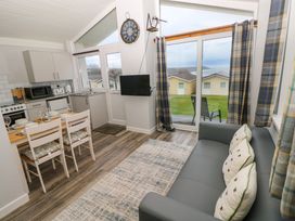 A kitchen and dining area with a table set for four next to a gray sofa and large sliding glass doors showing outdoor cabins at Chalet 22 in Port Eynon