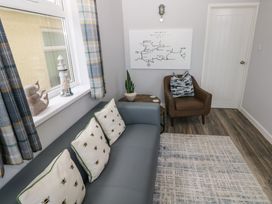 A seating area with a blue sofa with bee patterned cushions a brown armchair a small round wooden table a potted plant a wall map and a window with plaid curtains at Chalet 22 in Port Eynon