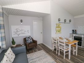 A living and dining area with a gray sofa a brown chair a wooden dining table with white chairs and kitchen appliances at Chalet 22 Port Eynon