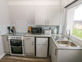 A kitchen with a white stove microwave fridge toaster kettle sink and window at Chalet 22 in Port Eynon