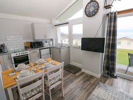 A kitchen and dining area with a wooden table set for four people and a wall mounted TV at Chalet 22 in Port Eynon