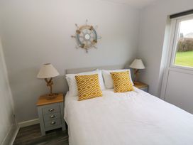 A bedroom with a white bed and yellow patterned pillows two bedside tables with lamps and a window showing a green lawn at Chalet 22 in Port Eynon