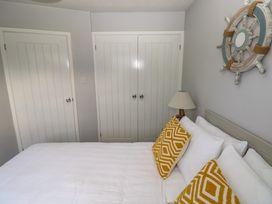 A bedroom with a bed with white linens and yellow pillows two white closet doors a white door a lamp and a wall decoration shaped like a ship wheel at Chalet 22 in Port Eynon