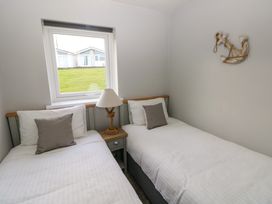 A bedroom with two single beds separated by a nightstand with a lamp and a window above the beds at Chalet 22 in Port Eynon