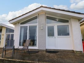 The front exterior of a small house with two outdoor chairs on a concrete patio at Chalet 22 in Port Eynon