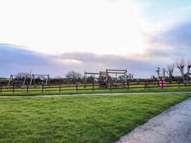 A playground with swings slides and climbing frames enclosed by a wooden fence with grassy areas at Chalet 22 in Port Eynon