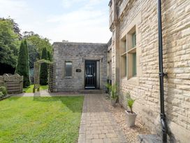 A stone building entrance with a black door potted plants along a brick pathway and tall trees in the background at Walworth Castle Lodge in Walworth near Darlington
