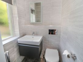 A bathroom with a white sink and dark cabinet under a mirror a white toilet with a toilet brush and toilet paper holder on the side at Walworth Castle Lodge in Walworth near Darlington
