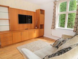 A living room with a mounted TV and wooden cabinets and a beige sofa with cushions at Walworth Castle Lodge in Walworth near Darlington