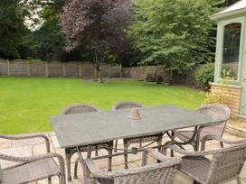 A garden patio with a stone table and six wicker chairs surrounded by grass and trees at Walworth Castle Lodge in Walworth near Darlington