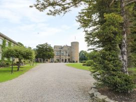 A gravel driveway leading to a stone castle with a round tower surrounded by trees and grass at Walworth Castle Lodge in Walworth near Darlington