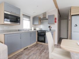 A kitchen with grey cabinets and appliances including microwave oven toaster and kettle with dining table and chair at Plot LD19 in Heysham