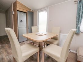 A dining area with a wooden table and four cream chairs near a silver refrigerator and a door at Plot LD19 Heysham