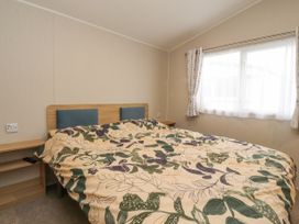 A bedroom with a double bed with floral bedding next to a window with curtains at Plot LD19 Heysham