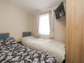 A bedroom with two single beds beside a window with curtains and a wall-mounted TV at Plot LD19 in Heysham