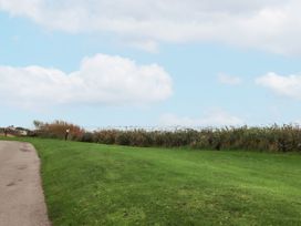 A paved pathway beside a green grassy area with bushes and a wire fence under a blue sky at Plot LD19 in Heysham