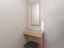 A small corner with a wall-mounted wooden shelf a rectangular wall mirror and a black cushioned stool at Plot LD19 in Heysham