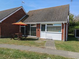 A single-story brick house with a tiled roof a white door and windows a patio table with chairs and an orange umbrella on the lawn at 1 Kessingland Cottages in Kessingland