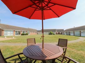 An outdoor wooden table with chairs and a red umbrella in a grassy courtyard surrounded by single-story buildings at 1 Kessingland Cottages in Kessingland