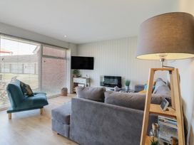 A living room with a grey sofa a teal chair a floor lamp and a TV mounted on the wall at 1 Kessingland Cottages in Kessingland