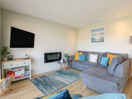 A living room with a gray sectional sofa with colorful cushions a wall mounted television wooden floor and a small console table with board games at 1 Kessingland Cottages in Kessingland