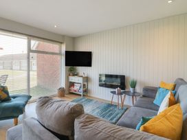 A living room with a gray sofa and colorful cushions a wall-mounted tv and a small table holding games at 1 Kessingland Cottages in Kessingland