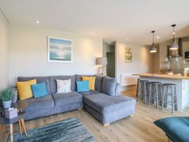 A living room with a gray sectional sofa and colorful cushions near a kitchen island with three stools at 1 Kessingland Cottages in Kessingland