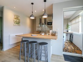 A kitchen with a wooden counter and three metal stools with a utility room visible through a glass door at 1 Kessingland Cottages in Kessingland