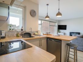 A kitchen with wooden countertops a sink a stove and hanging lights next to a living area with a sofa and a wall mounted TV at 1 Kessingland Cottages in Kessingland