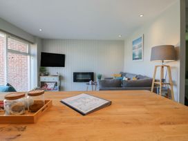 A living room with a grey sofa a wall-mounted tv a small table with board games and a wooden lamp at 1 Kessingland Cottages in Kessingland