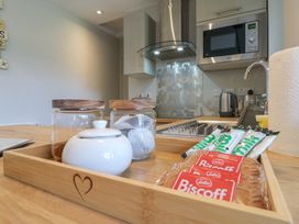 A kitchen counter with a wooden tray containing jars, tea bags, biscuits, and sachets next to a microwave and kettle at 1 Kessingland Cottages in Kessingland
