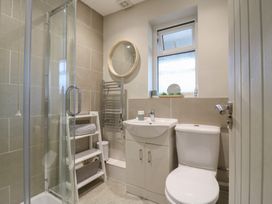 A bathroom with a shower enclosure sink toilet round mirror and storage shelves at 1 Kessingland Cottages in Kessingland