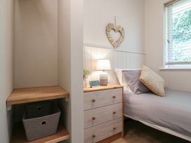 A bedroom with a bed next to a wooden dresser with a lamp and a heart-shaped wall decoration at 1 Kessingland Cottages in Kessingland