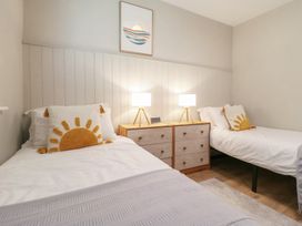 A bedroom with two single beds each with a sun design pillow and a wooden twin dresser with lamps between the beds at 1 Kessingland Cottages in Kessingland