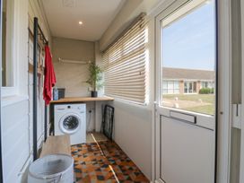 A utility room with a washing machine wooden shelf plant window blinds patterned carpet and a door to the outside at 1 Kessingland Cottages in Kessingland