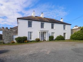 A white two-story house with multiple windows and chimneys surrounded by bushes and gravel driveway at Flat 3 in Trearddur Bay