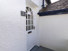 An exterior white door with glass panels and a mailbox slot next to a pebbledash wall with number 3 on a plaque at Flat 3 in Trearddur Bay