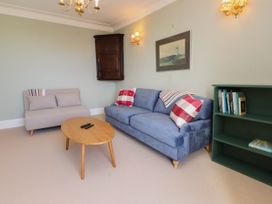 A living room with a blue sofa and a beige chair a wooden coffee table a green bookshelf and a framed picture on the wall at Flat 3 Trearddur Bay