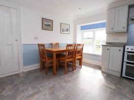 A kitchen dining area with wooden table and chairs near a window and white cabinets at Flat 3 in Trearddur Bay