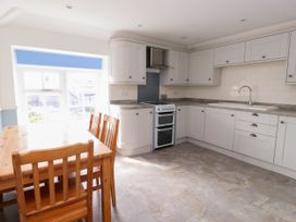 A kitchen with white cabinets a wooden dining table with chairs and a window with a blue blind at Flat 3 in Trearddur Bay